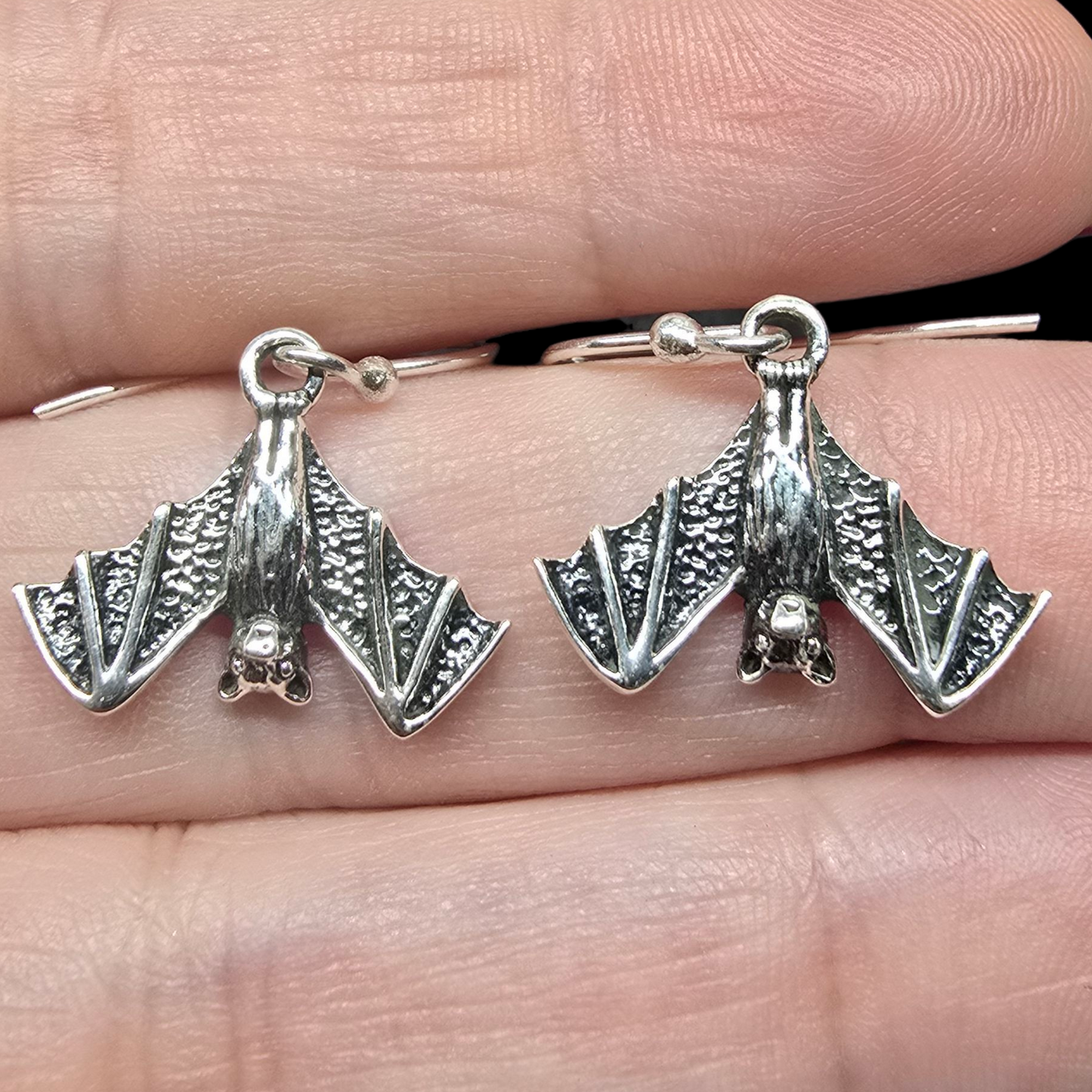 Silver bat-shaped earrings held between fingers