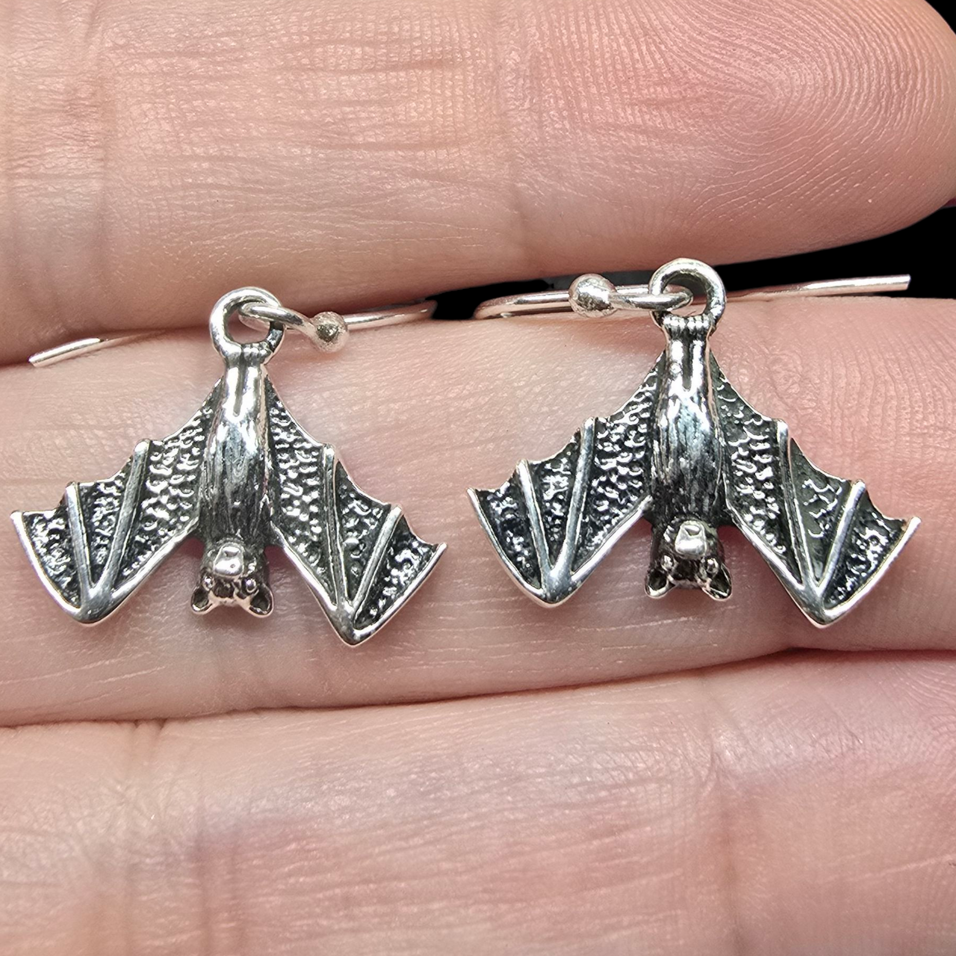 Silver bat-shaped earrings held between fingers