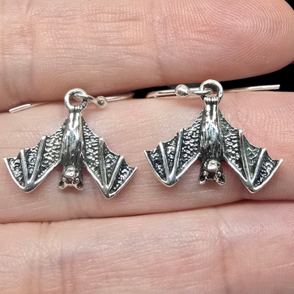 Silver bat-shaped earrings held between fingers